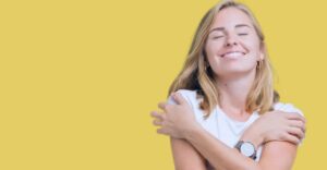 Women smiling and hugging herself on a yellow background
